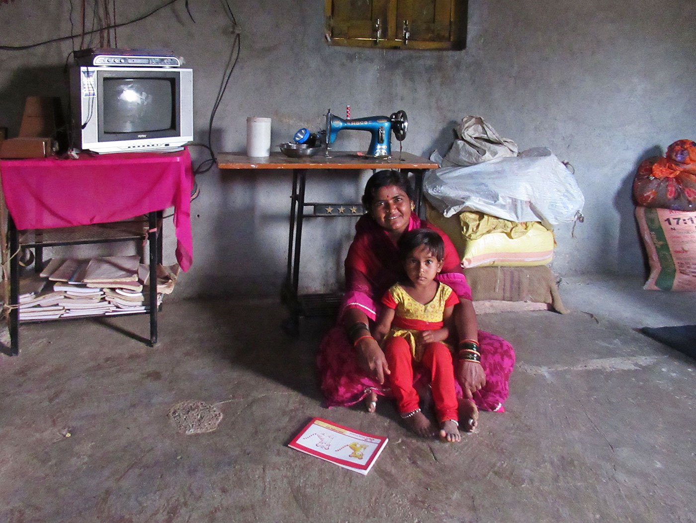 A woman sitting on the floor of her home with a young girl in her lap