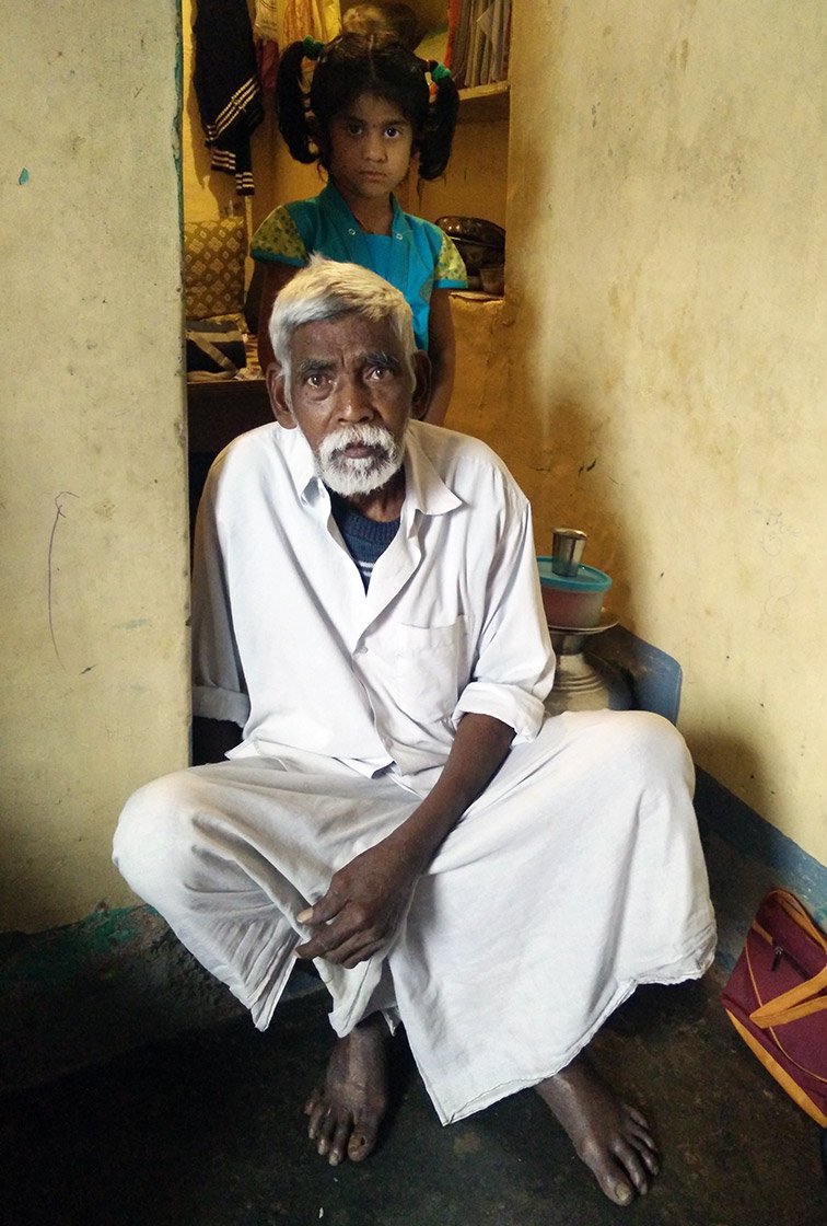 An elderly man sitting on the floor with a young girl standing behind him