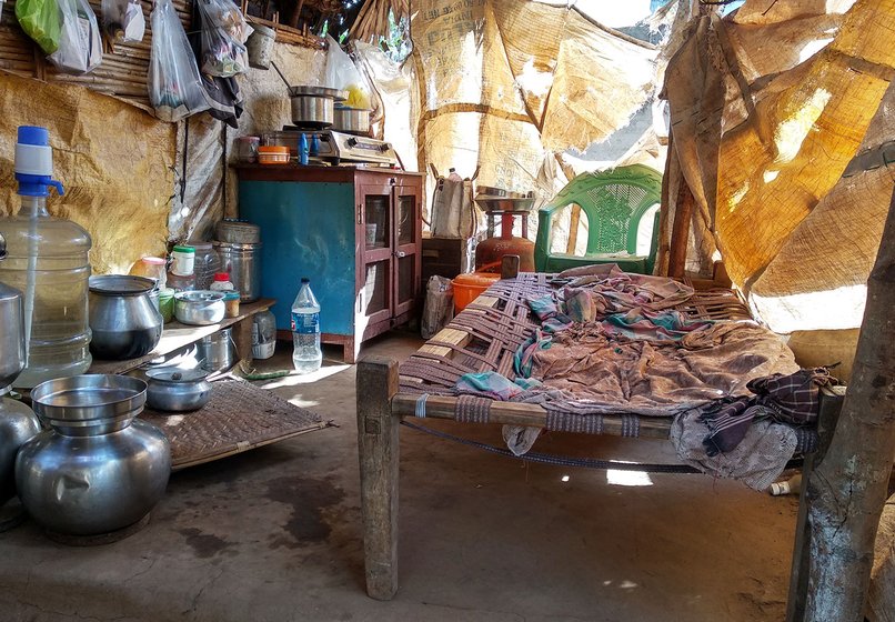 The remaining rooms of the house are covered with tarpaulin sheets. There is a bed and some vessels piled up in this room