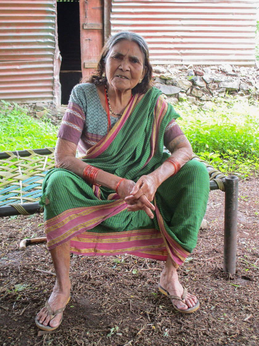 Gunamay sitting on a metal cot in her courtyard