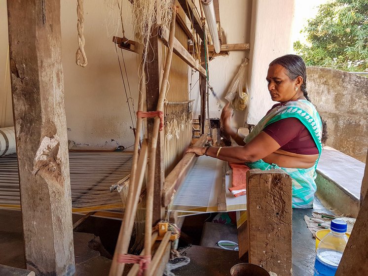 Jaya Mani works on a loom in her home. In the dying light of the setting sun, the threads on her loom glow faintly.