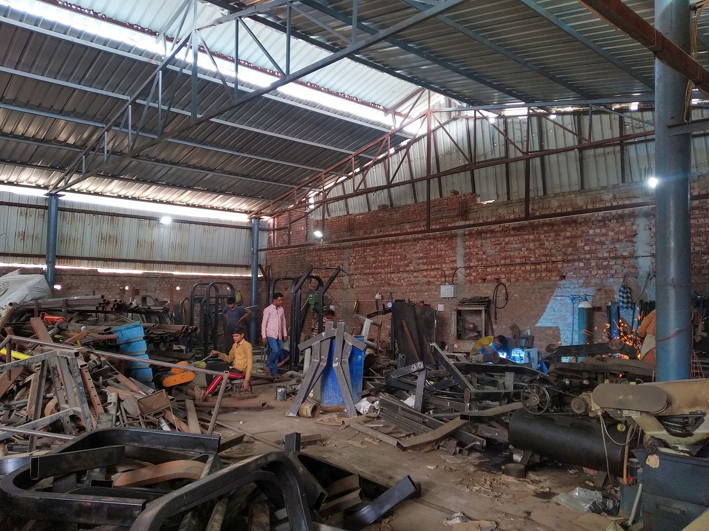 The factory workers dressed in colourful t-shirts operate electric machines that radiate sparks when brought in contact with metal