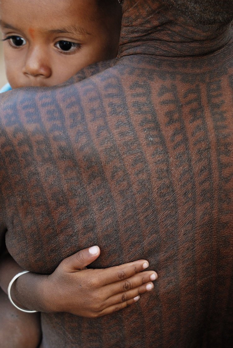 A man, with the name of Ram tattooed all over his body, holding a child.